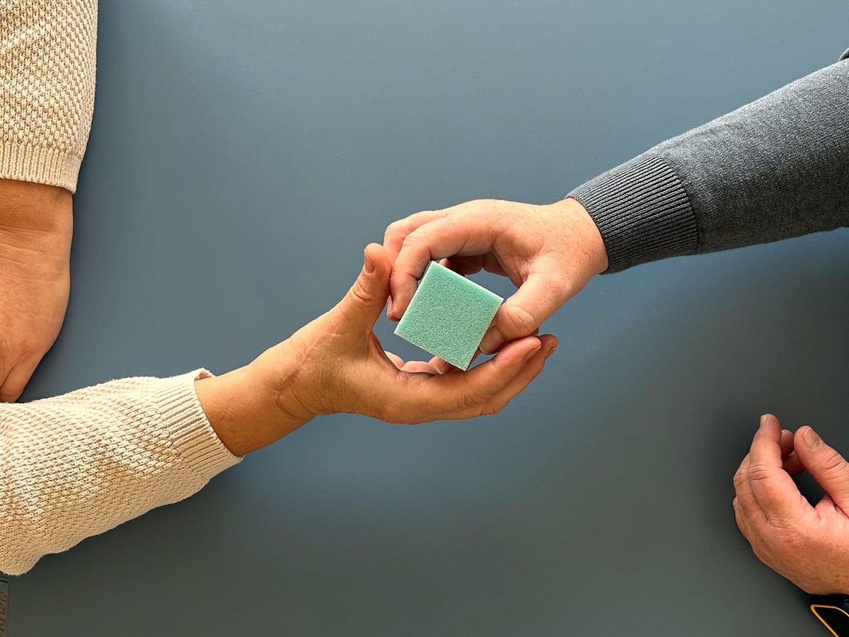 Greifübung am Tisch: ein Würfel wird von Hand zu Hand gereicht