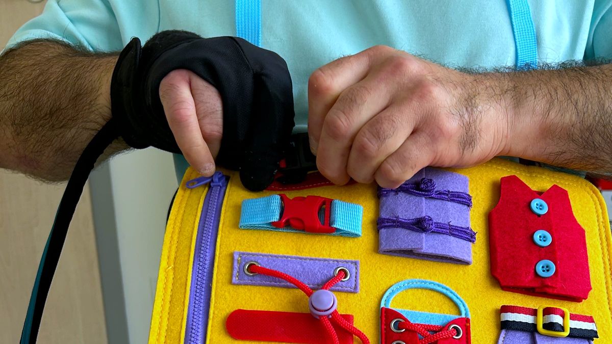Hände üben am Anziehtrainer das Schließen einer Schnalle