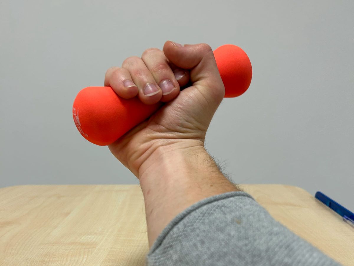 Hand hebt eine kleine Hantel über dem Tisch
